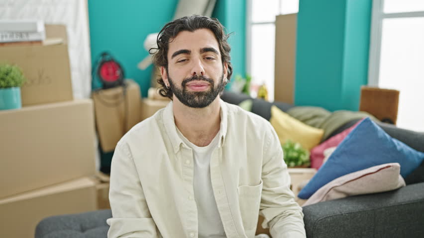 Young hispanic man smiling confident pointing to new home paper at new home