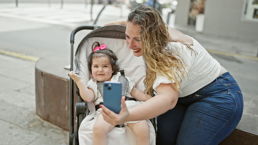 Mum and daughter making confident, smiling selfie with smartphone on city street, enjoying casual, fun family time outdoors