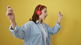 Young woman listening to music and dancing over isolated yellow background