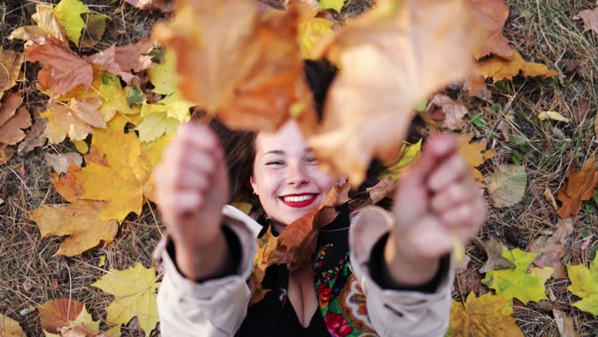 The girl lies on the yellow fallen leaves and leaves fall on her. Autumn concept.