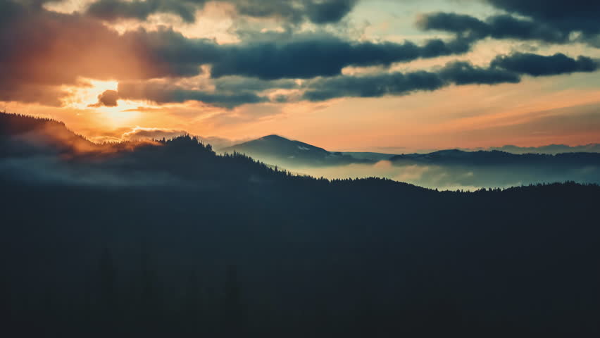 Epic foggy colorful sunrise in alp mountains. Dramatic clouds flow in bright sky, sun glow rising over mountain peak with golden light beams. Beautiful morning nature summer landscape. Time lapse