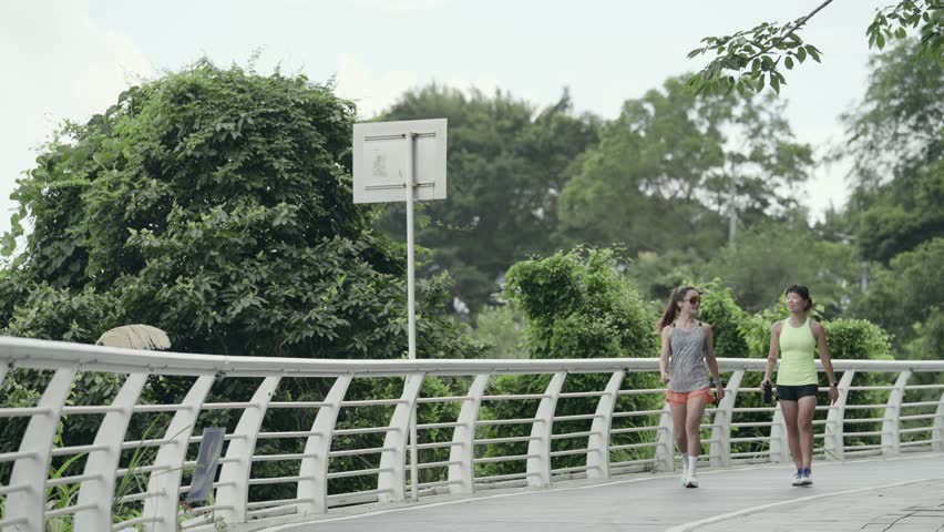two young asian women friends walking relaxing talking while exercising outdoors in park
