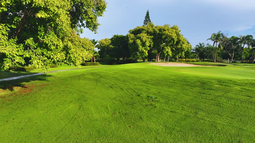 Short cut grass lawn in a tropical golf park and blue sky. Outdoor sport and lifestyle concept. Landscape of a golf course. A green lawn and a beautiful view of the sky over a lawn with palm trees.