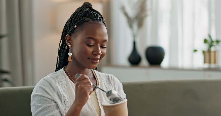 Black woman on couch, eating ice cream and relax in living room with smile, summer pleasure and enjoy. Happiness, fun or thinking, girl on sofa with taste of frozen chocolate gelato dessert in home.