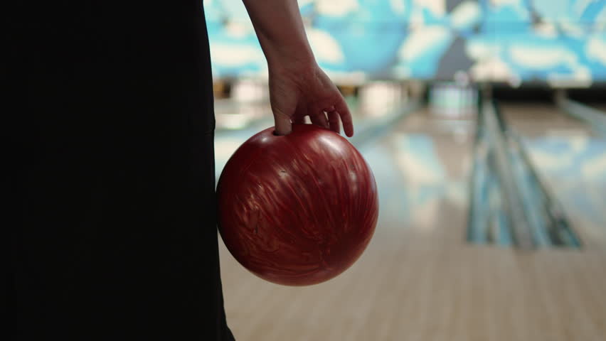 Bowling ball in female hand before throw indoor closeup. Woman holds standard heavy pearl colored ball in front of ready free lane, preparing to knock down pins. Royalty-Free Stock Footage #1110547775