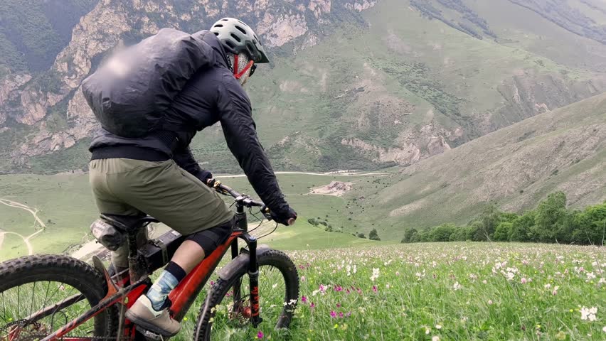 Bicyclist man riding mountain bike down cross country mountains slope covering green grass. Professional e-bike biker in protective equipment with backpack practicing extreme freeride bicycle 4k Royalty-Free Stock Footage #1110548881