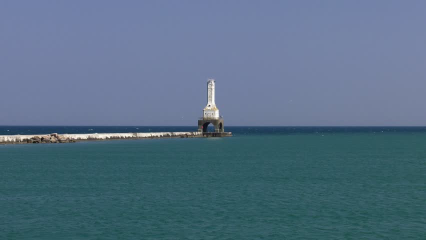 Port Washington lighthouse on Lake Michigan. Long shot from the shore pushes in to the lighthouse and its pier. Numerous gulls flying in the area. Shot on a smoky overcast day.