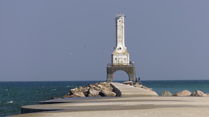 Port Washington lighthouse on Lake Michigan. Medium close shot of the lighthouse on its pier, with waves breaking over top. Shot on an overcast day as Canadian wildfire smoke moves in.