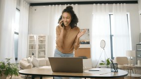 Young adult Afro American female entrepreneur working on laptop and speaking with client or partner on smartphone in home office. Positive small business owner managing project and multi tasking 4K - Powered by Shutterstock - Get 15% off with code: PIKWIZARD15