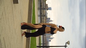 belly dancer outdoor with red flower in her fixed hair performing moving like a snake waves and sharp movements black dress revealing body red heels great city London in the background fence river sky - Powered by Shutterstock - Get 15% off with code: PIKWIZARD15