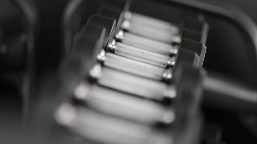 Slow motion close up of woman picking up free weight from dumbbell rack at fitness center