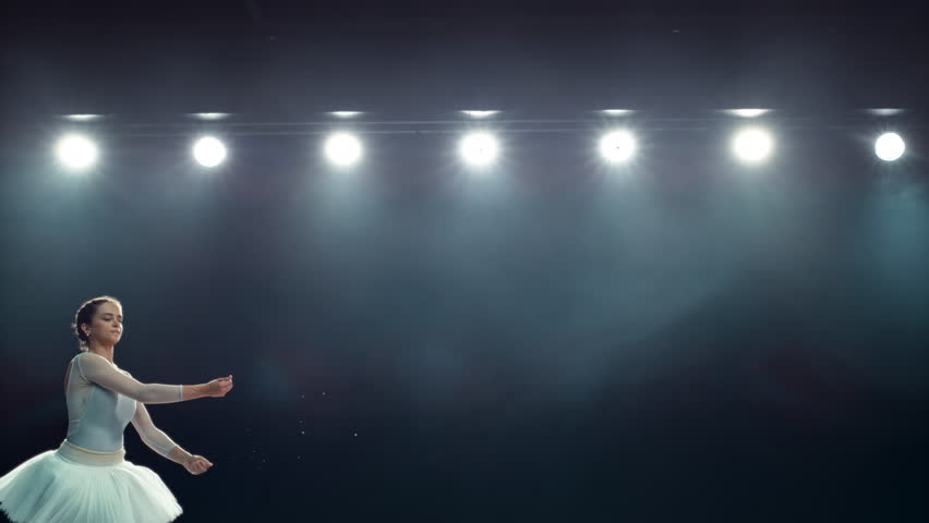 Beautiful Ballet Performance on a Big Stage with Lights. Young Female Ballerina in White Dress Making a Perfect Split Leap and Releasing Powder. Super Slow Motion Speed Ramp Effect