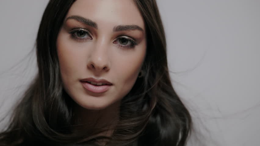 A young charming brunette woman with wind-blown hair posing on a light gray background.