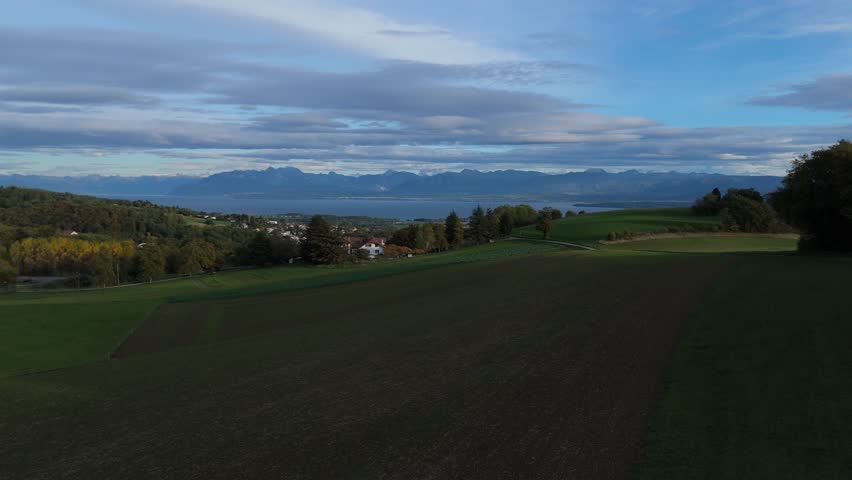 Aerial view of farmhouse, crops, hills, trees and farmer playing with his dog. Great view of Lake Geneva and the Swiss Alps in the background.