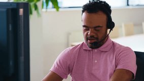 Man with Down Syndrome wearing headset sitting at desk working in office call centre team - shot in slow motion - Powered by Shutterstock - Get 15% off with code: PIKWIZARD15