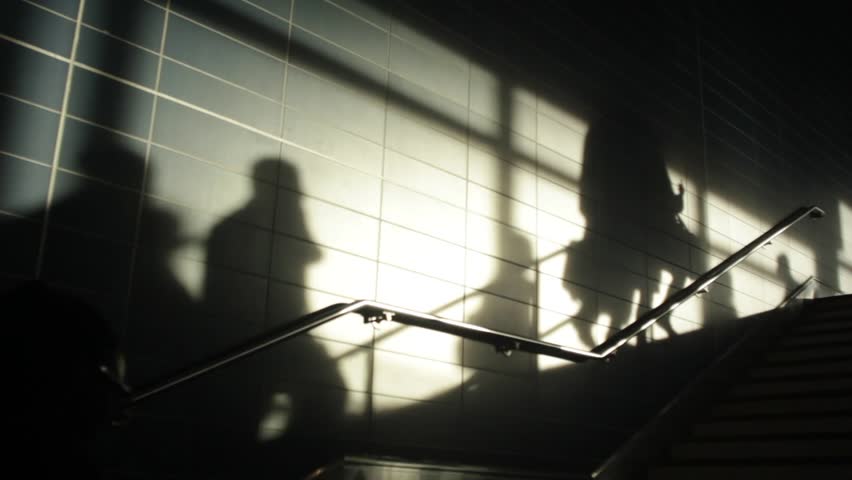 Crowd of silhouetted pedestrians, people of all ages walking at sunset against the sun creating long shadows.