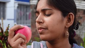 Happy young girl biting an apple at home. Beautiful Asian young woman eating fresh apple fruit outdoors. Healthy fresh food and vegetarian dieting concept. 4k video.