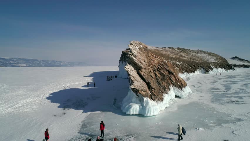 Aerial view on the rocky ice covered island in lake Baikal. Groups of tourist walking around on the cracked ice. Famous tourist spot. Beautiful winter landscape of lake Baikal