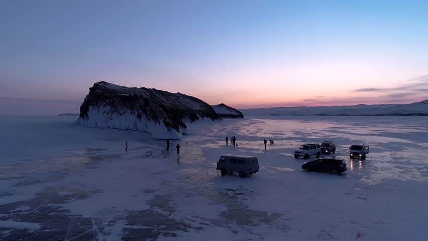 Aerial winter landscape of frozen lake Baikal. Groups of tourists got off the cars and walking around the rocky island in lake Baikal, walking on the crystal clear ice at sunrise. Famous tourist spot