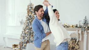 Happy couple having fun dancing a dance holding hands in living room at home during winter New Year Christmas Xmas holidays. Wife and husband are circling in dance, smiling. They have a festive mood - Powered by Shutterstock - Get 15% off with code: PIKWIZARD15