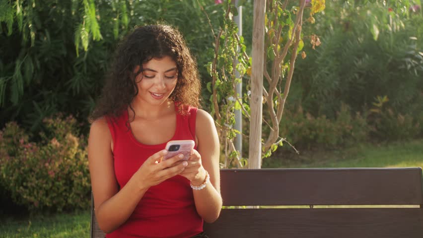 Blissful happy beatiful hispanic woman holding using cell phone in the street of city. Smiling young latin woman blogger brosing social media, buying in internet, ordering products online in apps.