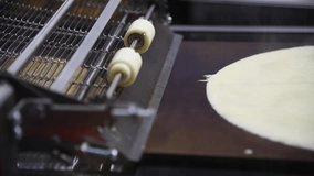 Close-up view of working automated thin pancake frying machine in fast food restaurant or pancake shop. Soft focus. Real time handheld video. Food technology theme.