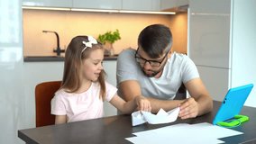 Father and little daughter build origami white paper boats use video tutorial on tablet at home. Happy family plays handmade boats. Crafts, diy. Leisure