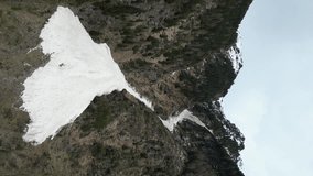 Aerial view of an avalanche in the mountains. Vertical video of natural dangerous processes of snow climbing from mountain slopes. High quality 4k footage
