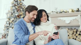Smiling couple is shopping in online store using smartphone sitting on sofa in living room at home during winter New Year Christmas Xmas holidays. Husband and wife are happy with discounts and sales - Powered by Shutterstock - Get 15% off with code: PIKWIZARD15