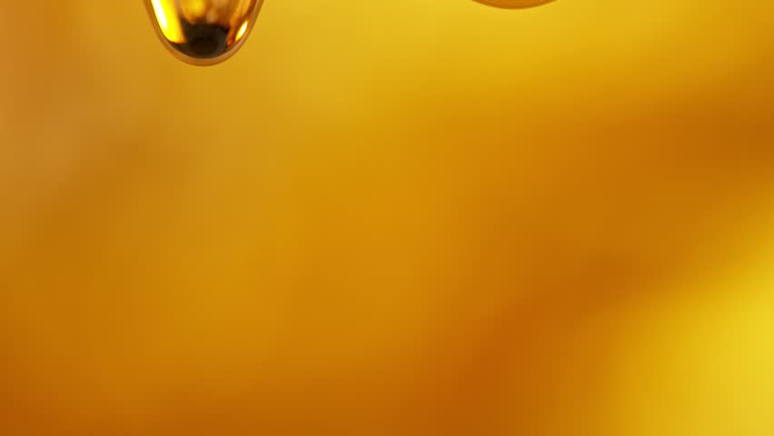 Super Slow Motion Shot of Falling Golden Oil Droplets Isolated on Orange Background at 1000 fps.