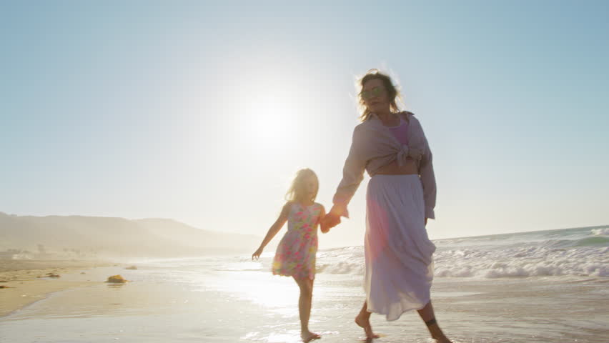 Cinematic silhouettes of mother running with cute happy daughter by sandy beach. Kid dream of traveling on summer vacation. Carefree girl having fun time together with mother at ocean. Happy family 4K Royalty-Free Stock Footage #1110594141