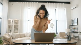 Positive small business owner managing project and multi tasking 4K. Young adult Afro American female entrepreneur working on laptop and speaking with client or partner on smartphone in home office - Powered by Shutterstock - Get 15% off with code: PIKWIZARD15