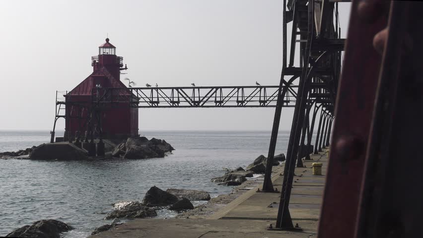 Sturgeon Bay lighthouse on Lake Michigan. Static medium shot along the pier outside of the catwalk uprights from close to the shore. Shot on a very overcast day as Canadian wildfire smoke moves in.