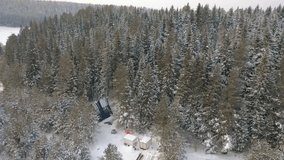 Aerial of magic snowy winter wonderland with a small glamping unbuilt house among trees. Clip. Winter season in snowy mountain forest.