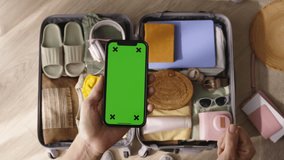 Top view smartphone with green chroma key in hand woman. Green screen phone, meticulously packed luggage. Mockup of mobile app for organizing to-dos, plans, lists, assistant. Stress-free weekend trip