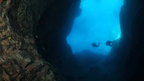  scuba divers exploring reefs underwater deep blue water big rocks and bubbles ocean scenery with some fish