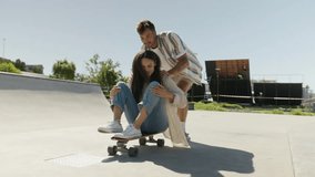 Young multiracial couple in casual clothing having fun on skateboard at the skatepark