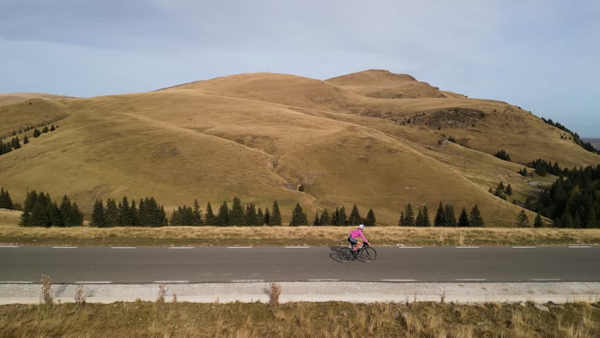 Aerial drone view of road cyclist riding a bike in mountains. Cyclist riding bicycle in mountains. Cycling and triathlon concept. Healthy outdoor lifestyle for athletes. Woman rides bike at fall.