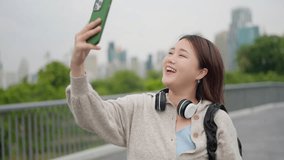 Happy young asian woman video call through smartphone at public park. Charming female in casual clothes talking on video call through mobile phone while relaxing in the park. Technology concept