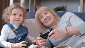  Happy modern grandmother with little granddaughter playing computer game together. 