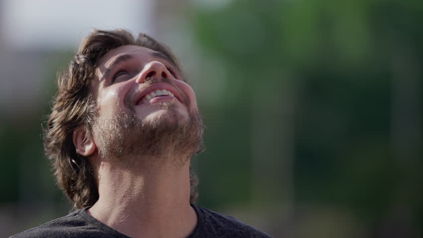 One happy young man looking up at sky with HOPE and FAITH. Smiling male person gazes up with GRATITUDE outdoors in tracking shot close up face Royalty-Free Stock Footage #1110611623