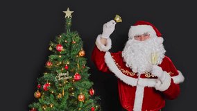 Santa Claus with a glass of sparkling wine stands next to the Christmas tree. Rings the bell on a black background. - Powered by Shutterstock - Get 15% off with code: PIKWIZARD15