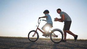 Father's Day. Father teaches son to ride bicycle wearing safety helmet. child learn to ride bicycle in park at sunset. Happy family concept and dream. Active father teaches child to ride bike in park - Powered by Shutterstock - Get 15% off with code: PIKWIZARD15