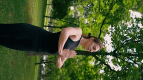 vertical video an experienced female instructor meditates in the park practices yoga does stretching and exercises different muscle groups