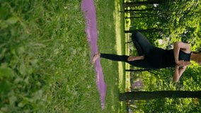 vertical video an experienced female instructor meditates in the park practices yoga does stretching on one leg and exercises different muscle groups