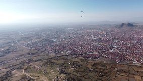 Person paragliding over eastern european town. Aerial drone video of Prilep in North Macedonia.