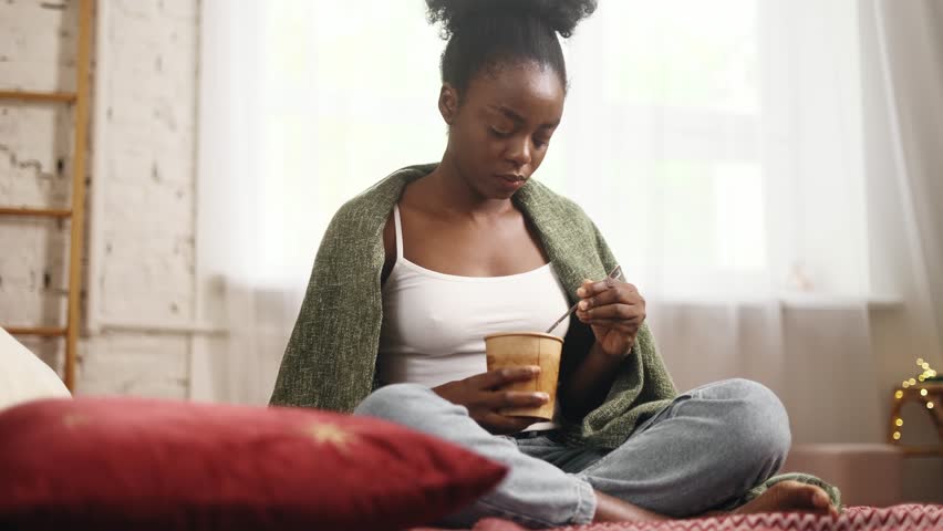 Portrait of sad young woman dealing with stress by eating food sitting on bed at home Upset brunette female wrapped in blanket crying and eating ice cream indoors alone Mental heath problem Royalty-Free Stock Footage #1110628759