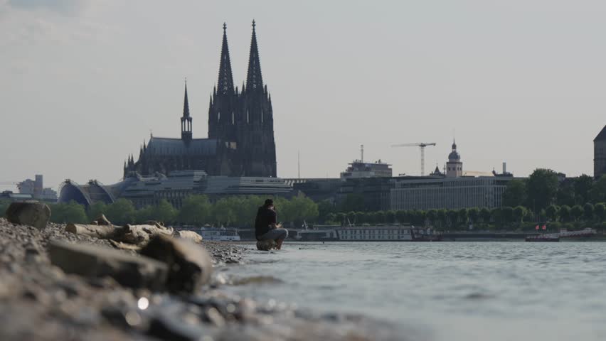 Unrecognizable young couple relaxing on Rhein river bank sitting with feet cooling in shallow water with breathtaking view of Cologne Dom cathedral at background Royalty-Free Stock Footage #1110628849