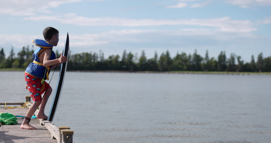 Young boy jumps off dock into lake water with boogy board - cottage fun