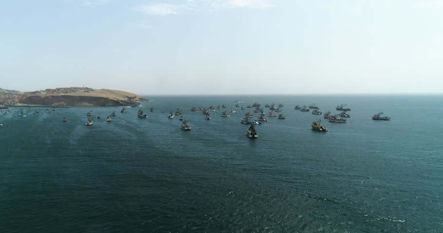 Aerial view approaching fishing ships anchored on the shore of sunny Huacho, Peru